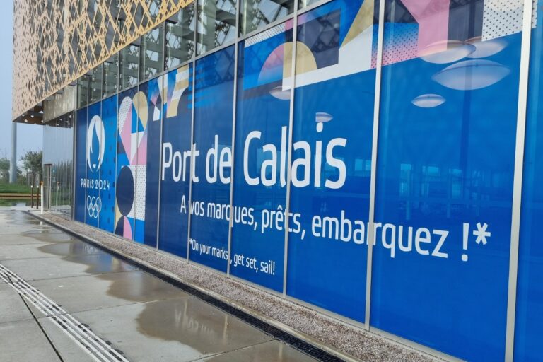 The side of the terminal building at the check-in is decorated with an advertisement for the Paris 2024 Olympic Games.